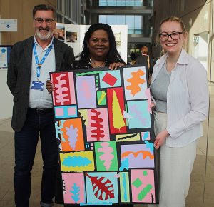 Three people from OutPost Arts, including Euan Macleod, holding artwork